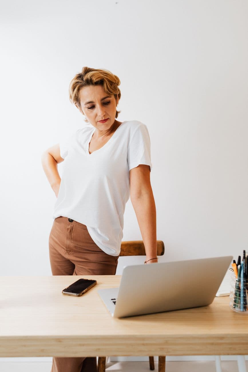 Personne assise à un bureau ergonomique ajusté, avec un écran à hauteur des yeux, un clavier et une souris positionnés pour éviter les tensions, dans un environnement de travail lumineux et spacieux.