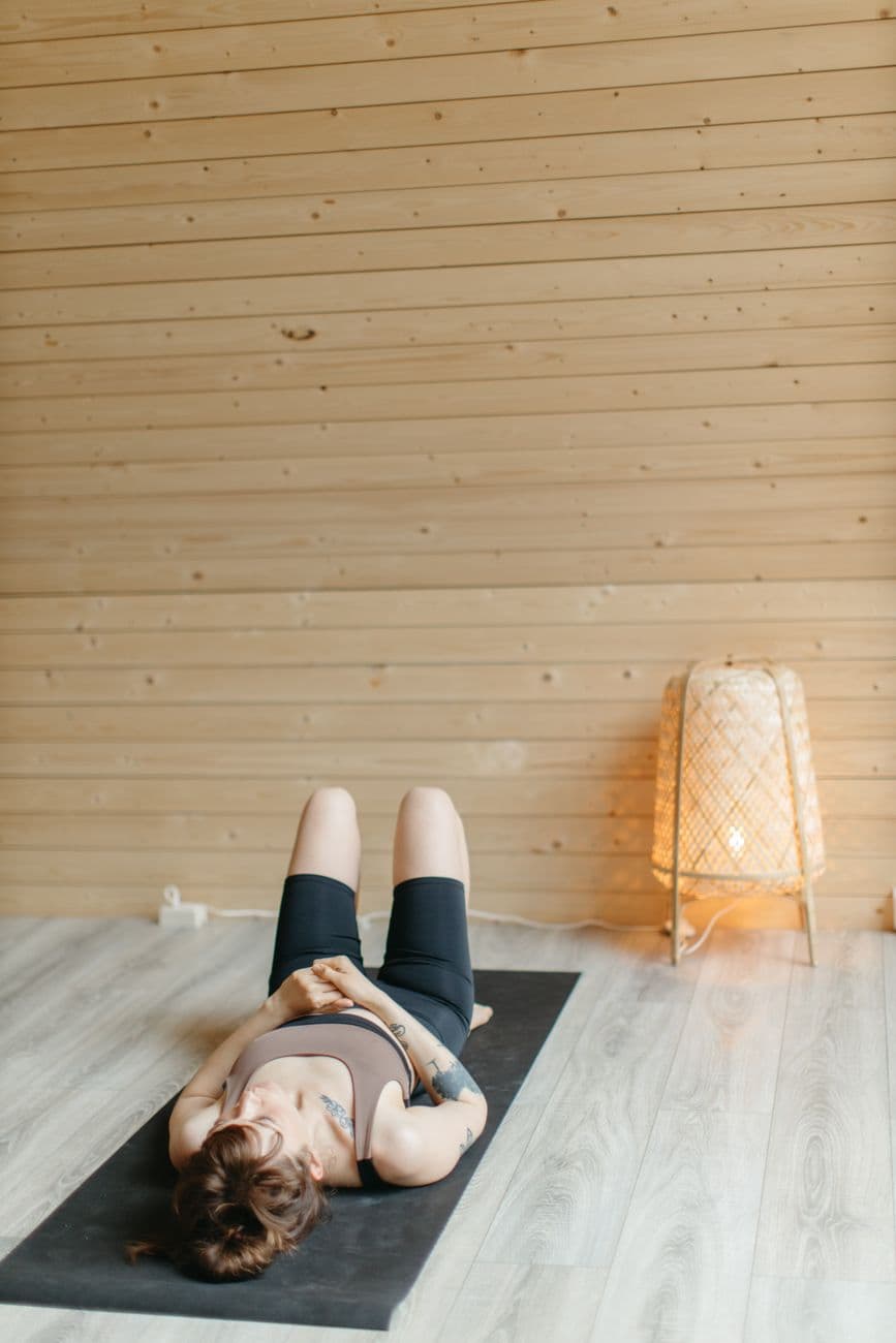 Femme d'âge mûr réalisant un étirement du psoas sur un tapis de yoga dans un salon lumineux, avec une posture détendue et un sourire apaisé.