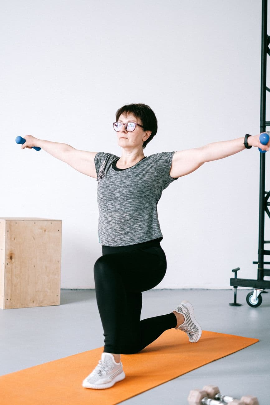 Une femme senior souriante en tenue de sport assise sur un tapis de yoga, effectuant un étirement doux des jambes avec l'aide d'une sangle, dans un salon lumineux.