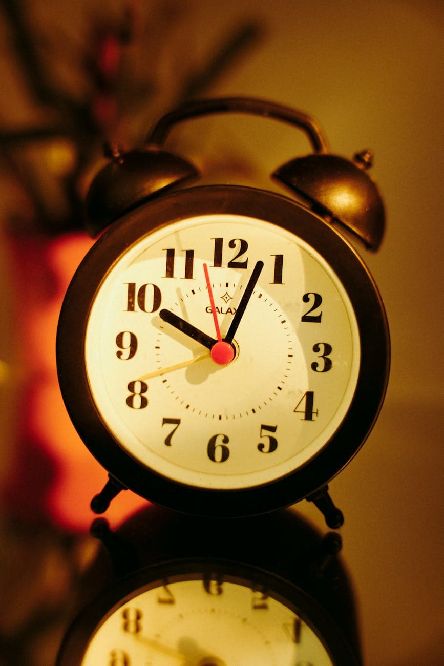Personne d'âge mûr assise paisiblement sur son lit dans une chambre tamisée, regardant par la fenêtre avec une tasse de tisane à la main, exprimant une ambiance de calme nocturne.