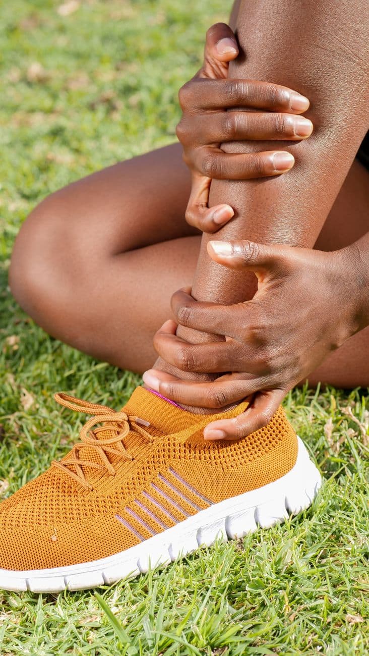 Personne d'âge mûr réalisant un exercice d'équilibre sur une jambe, avec une main posée sur le dossier d'une chaise pour se stabiliser, dans un environnement domestique.