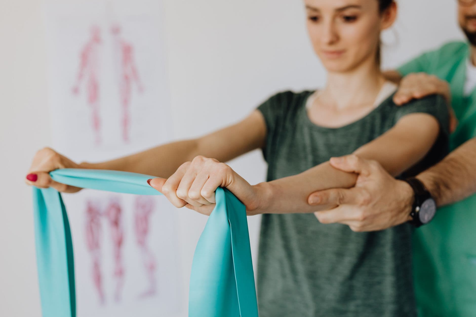 Personne d'âge mûr en tenue de sport légère, effectuant un exercice doux avec un élastique pour l'épaule, sous la supervision bienveillante d'un kinésithérapeute dans une salle de rééducation lumineuse.